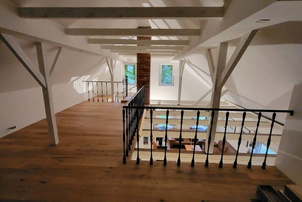 Een zolderkamer met houten vloeren, een zwart metalen hekwerk en een bakstenen muur.