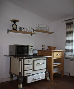 A kitchen with a microwave, a kettle, and shelves above holding glassware. - Rosenhof Grossefehn East Frisia (Grossefehn)