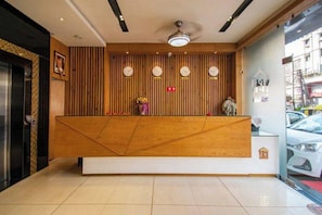 A reception desk with a wooden finish, a ceiling fan, and a wall-mounted clock. - Hotel Kiran Inn (Indore)
