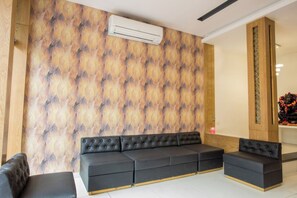 A modern interior with a sectional sofa, a wooden accent wall, and a built-in air conditioning unit. - Hotel Kiran Inn (Indore)
