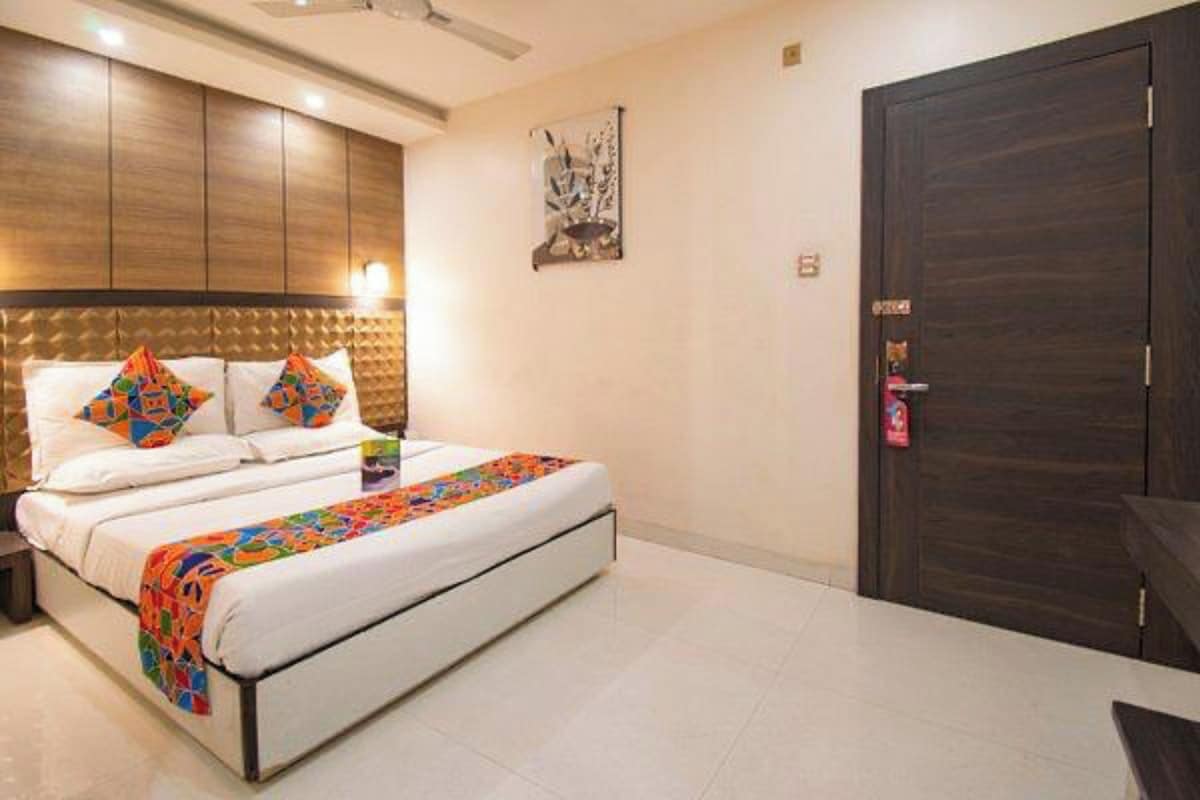 A hotel room with a bed, a nightstand, a dark wooden door, and a wall-mounted light fixture.