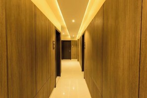 A corridor with wooden walls and a shiny floor, leading to a door at the end. - Hotel Kiran Inn (Indore)