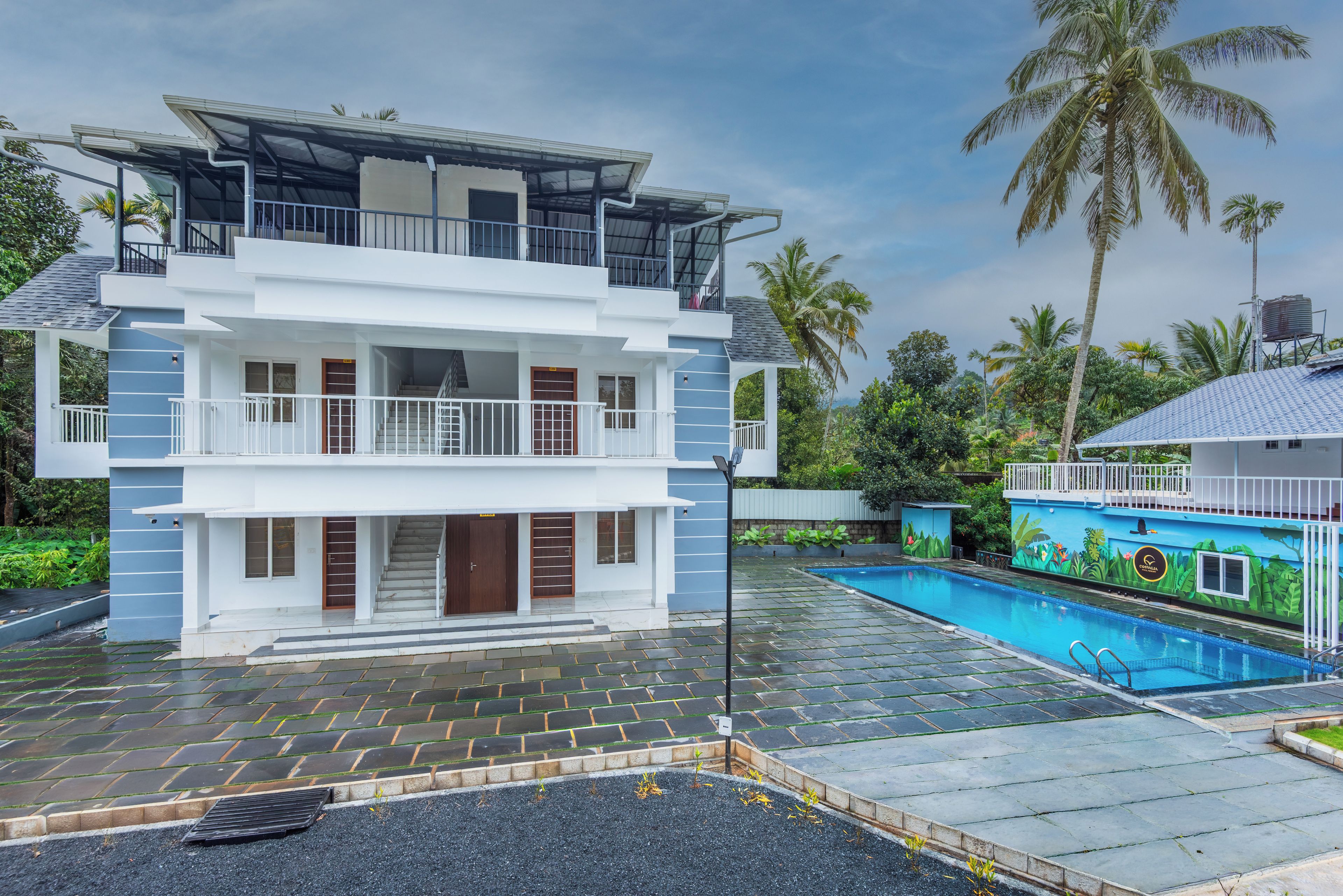 En toetagers bygning med balkon, swimmingpool og en tropisk have.