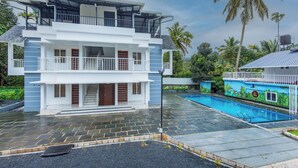 Un edificio a due piani con un balcone, una piscina e un giardino tropicale.