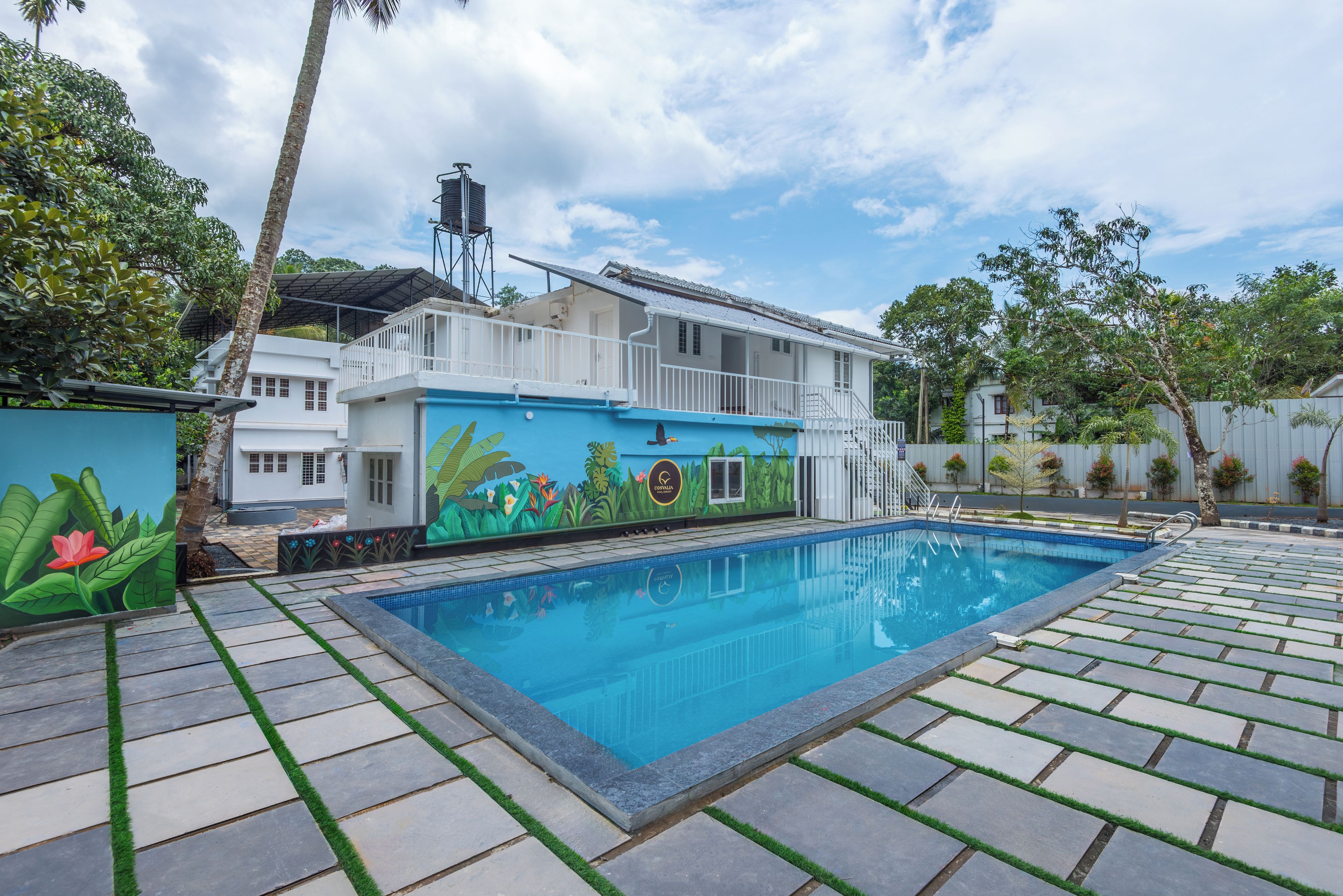 A swimming pool with a mural, a white building, and a water tower.