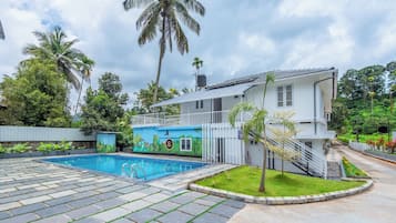Un edificio de dos plantas con piscina, rodeado de exuberante vegetación y palmeras.
