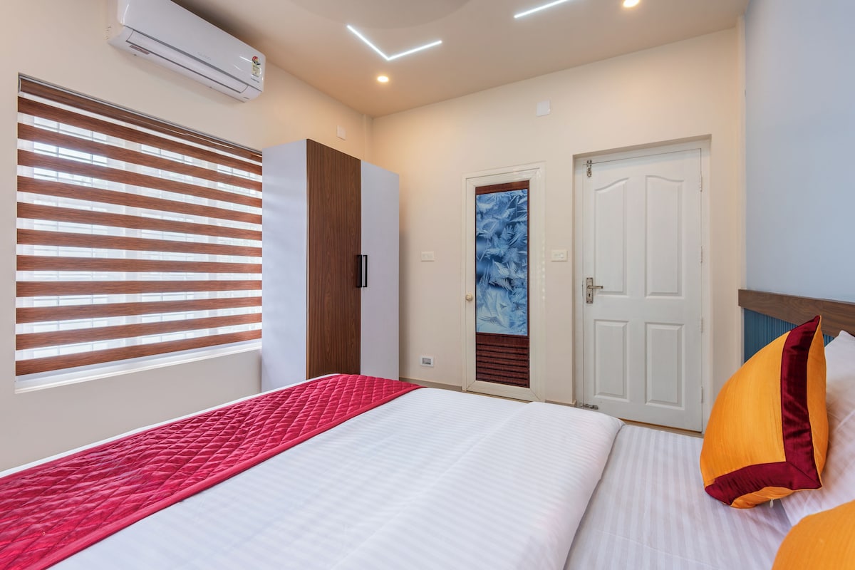Quarto com cama, guarda-roupa, porta com painel de vidro jateado e ar condicionado.