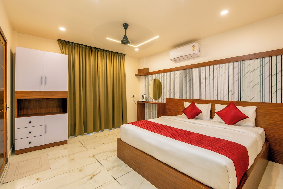 Quarto de hotel com cama, guarda-roupa, ventoinha no teto, aparelho de ar condicionado e janela com cortinas.