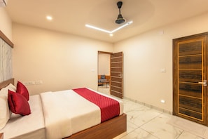 Habitación de hotel con cama, armario de madera, ventilador de techo y baño visible a través de una puerta abierta.
