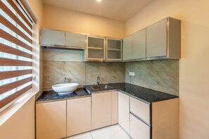 Cozinha compacta com pia branca, bancada escura e armários bege.