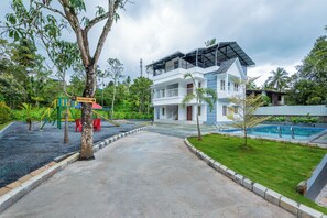 A two-story building with a reception area, a swimming pool, and a playground. - Cosvalia Pool Resort (Wayanad)