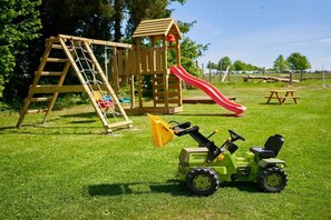 Een speeltuin met een glijbaan en klimconstructie, een picknicktafel en een tractor speelgoed.