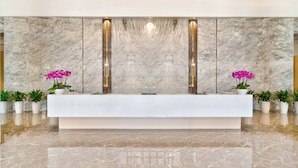 A reception desk with a marble wall background, two vertical light fixtures, and potted plants on either side. - Grand Skylight X-INN Inn Pingshan (Shenzhen)