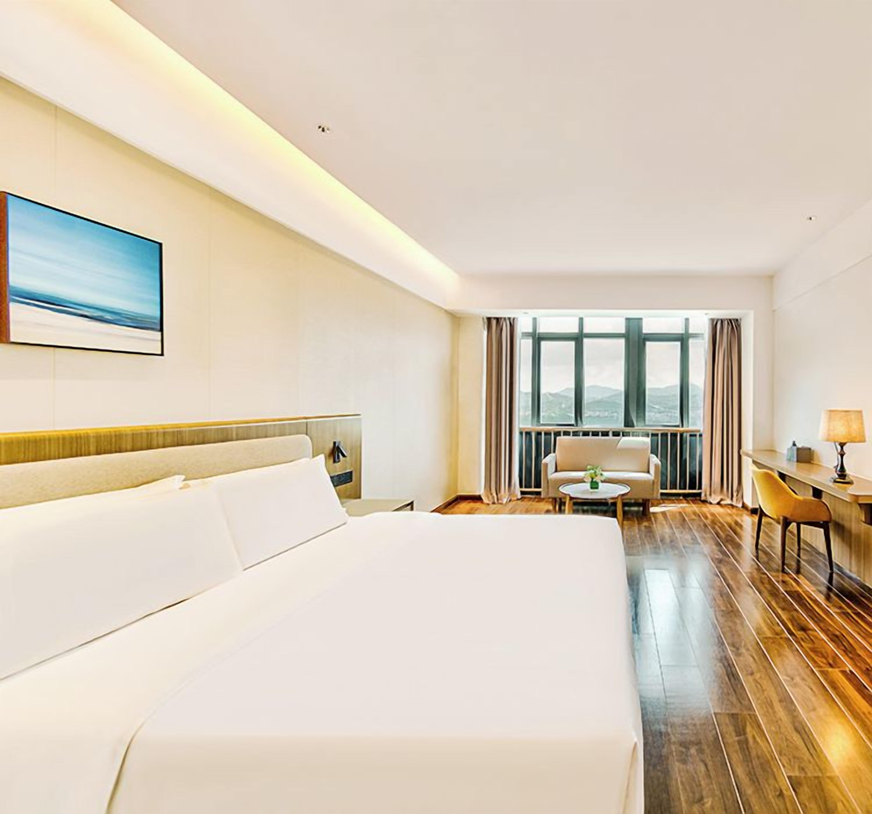 A hotel room with a large bed, a desk, a chair, and a view of the outdoors through a window.