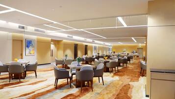 A hotel conference room with multiple tables and chairs, a patterned carpet, and a modern ceiling design.