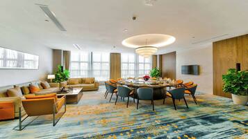 Una habitación de hotel moderna con zona de comedor, un conjunto de sofás y un amplio ventanal.