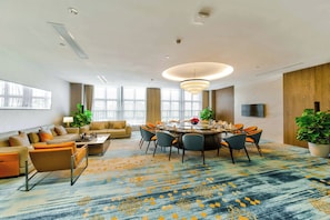 A modern hotel room with a dining area, a sofa set, and a large window.