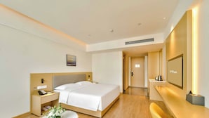 A hotel room with a bed, bedside table, lamp, and a small round table with a vase of flowers. - Grand Skylight X-INN Inn Pingshan (Shenzhen)