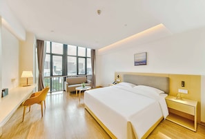 A hotel room with a large bed, a desk, a chair, a small table, and a view of the city through large windows. - Grand Skylight X-INN Inn Pingshan (Shenzhen)