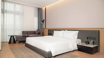 Ein modernes Hotelzimmer mit einem großen Bett, einer Couch, einem kleinen Tisch und einem Nachttisch mit einer Lampe.