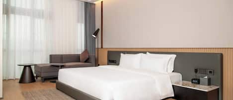 Et moderne hotelværelse med en stor seng, en sofa, et lille bord og et natbord med lampe.