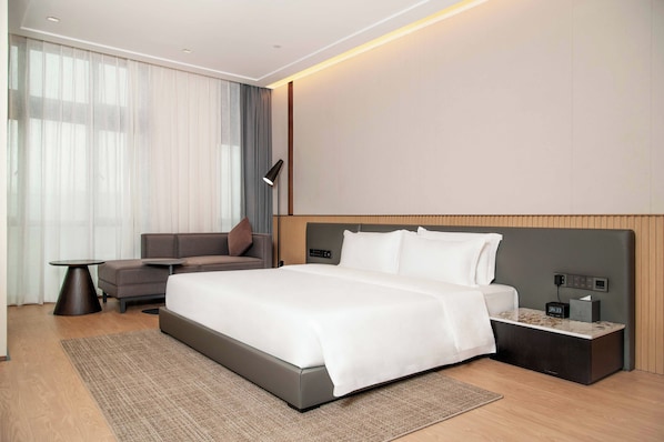 A modern hotel room with a large bed, a sofa, a small table, and a nightstand with a lamp. - Grand Skylight X-INN Inn Pingshan (Shenzhen)