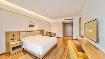 A modern hotel room with a large bed, bedside tables, a desk, a chair, a flat-screen TV, and a door leading to a bathroom.