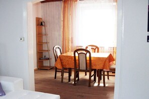 A dining area with a table and chairs, a wooden floor, and a window with curtains. - Holiday home with 1 bedroom (Bodenwerder)