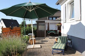 Eine Terrasse mit einem grünen Sonnenschirm, einer Bank und einem Tisch.