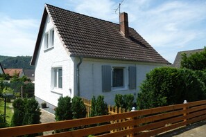 Ein zweistöckiges Haus mit einem Ziegeldach, einem Schornstein und einem Holzzaun.