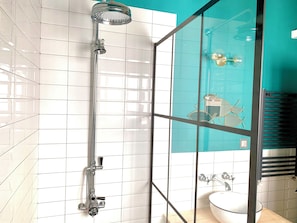 Un baño con cabina de ducha de vidrio, paredes de azulejos blancos, un lavamanos blanco y una pared de acento color verde azulado.