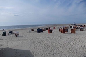 A beach with numerous small, colorful structures, possibly for storage or shelter, and a lifeguard tower in the distance. - Oskar in seaside villa Seagull's Nest (Borkum)