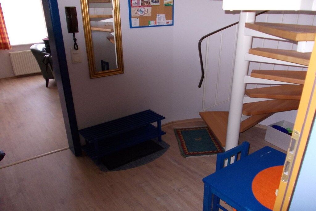 A room with a wooden staircase, a blue chair, a small blue table, and a mirror on the wall.