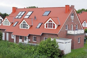 Een huis van rode baksteen met meerdere dakramen, een witte garage en een klein bijgebouw met een balkon.
