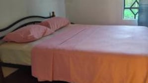 Una cama individual con colcha rosa en una habitación con ventana y cortinas.