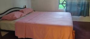 A single bed with a pink bedspread in a room with a window and curtains. - Henz and Sia Tourist Residence 2 — Your Peaceful Island Home in Rodrigues (Reposoir)