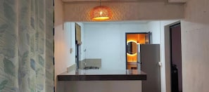 A kitchen with a modern design, featuring a hanging light fixture and a view into the adjacent dining area. - Henz and Sia Tourist Residence 2 — Your Peaceful Island Home in Rodrigues (Reposoir)
