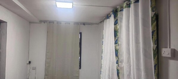 A room with a ceiling light, white walls, and a window with a curtain.