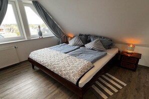 Een slaapkamer met een bed, een nachtkastje, een lamp, een raam met gordijnen en een radiator.