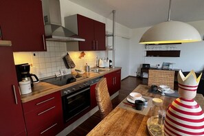 Eine moderne Küche mit roten Schränken, einer Holztischplatte und einem Essbereich mit Tisch für zwei Personen.