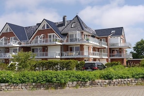 Een rij twee-onder-een-kaphuizen met meerdere balkons, een stenen muur ervoor en een verharde oprit.