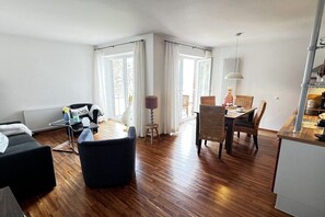 A modern living room with a black sofa, a small table, and a dining area with wicker chairs. - Holiday apartment with 1 bedroom (Cuxhaven)