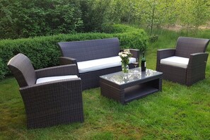 Eine Sitzgruppe im Freien aus Rattan mit einer Couch und zwei Stühlen, einem Glastisch und einer Vase mit Blumen.