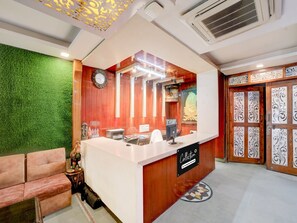 A reception area with a wooden reception desk, a green wall, a clock, and a decorative door with intricate patterns.