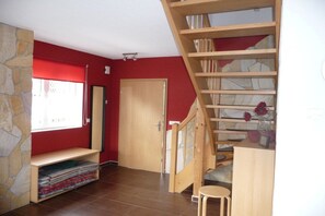 A room with a red wall, a wooden staircase, a stone wall, and a window with blinds. - Holiday home with 2 bedrooms (Altendorf)