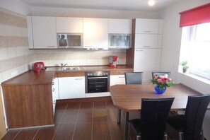 A modern kitchen with white cabinets, a wooden countertop, a built-in oven, and a dining area with a table and chairs. - Holiday home with 2 bedrooms (Altendorf)