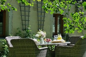 An outdoor dining area with wicker furniture, a table with fruit and a glass of lemonade, and a wall with a window and a ladder. - "Am Teich" on the Sanderhof (Rathmannsdorf)