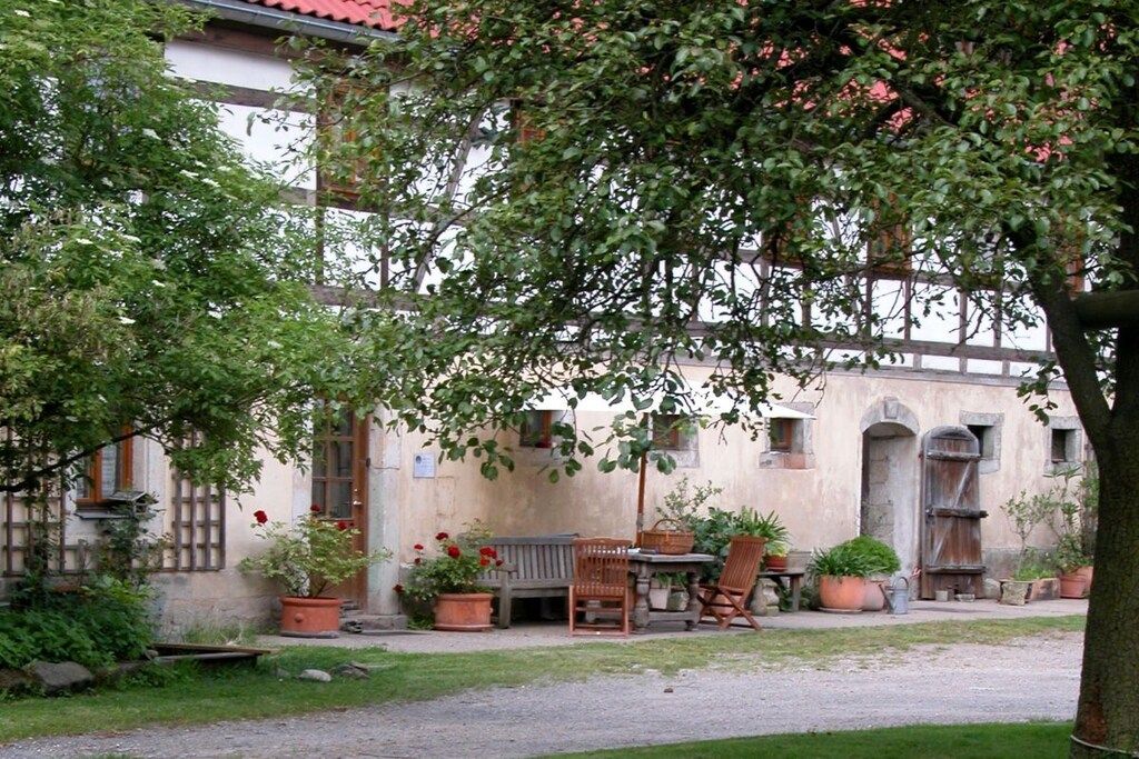 A courtyard with a rustic building, outdoor seating, and potted plants.