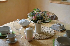 A round table with a woven placemat, a white teapot, a vase with flowers, and several cups and saucers. - "Am Teich" on the Sanderhof (Rathmannsdorf)