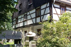 A traditional half-timbered building with a visible window and a stone structure in the foreground. - "Am Teich" on the Sanderhof (Rathmannsdorf)